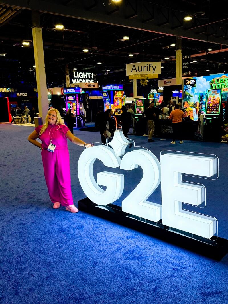 Jennifer Bowman in a pink jumpsuit beside the illuminated G2E sign on the show floor at G2E 2026 in Las Vegas.